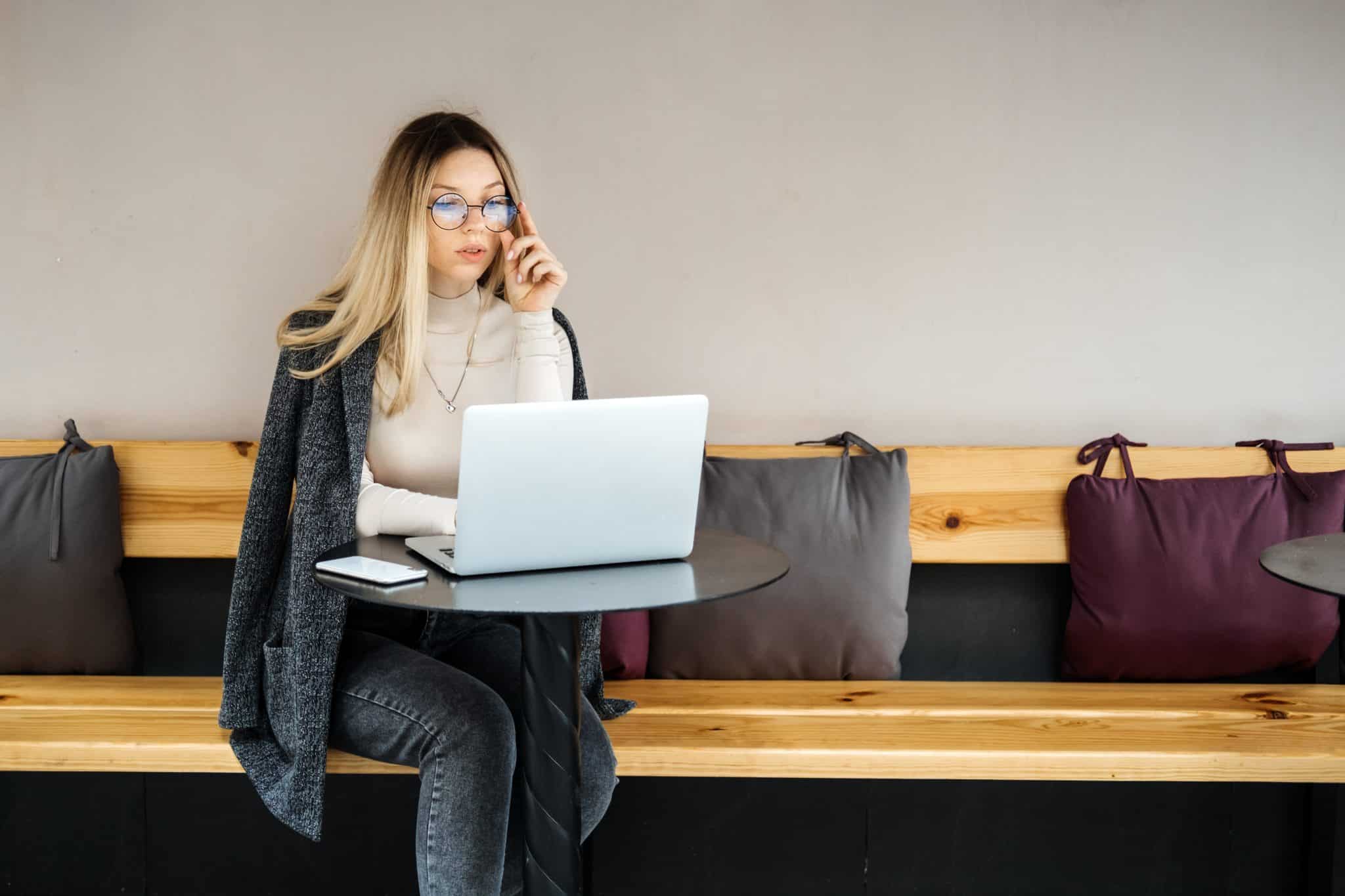 Woman on her phone and working on laptop in coffee shop